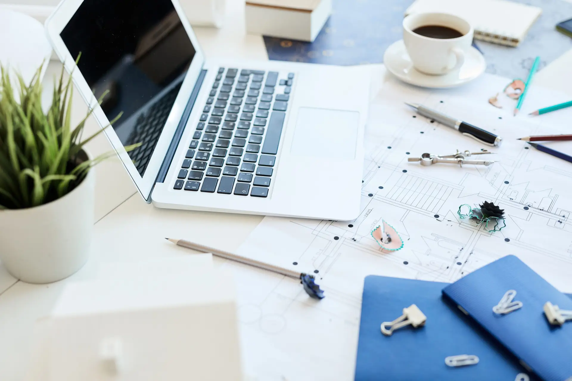 Close-up of engineering tools, sharpening shavings, paper clips and pencils on desk with portable computer and blueprint